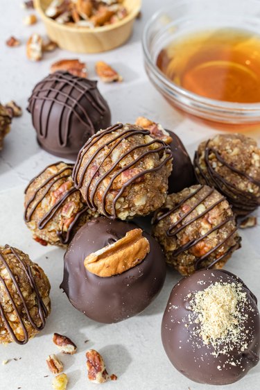 The pecan pie bourbon balls in a pile on a white counter next to a small glass dish of bourbon.