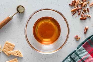 A small glass bowl filled with maple syrup, bourbon, and vanilla extra on a white counter.