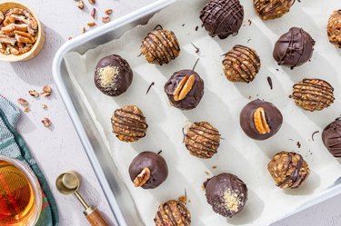 Pecan Pie Bourbon Balls on a parchment paper-lined baking sheet on a white counter.