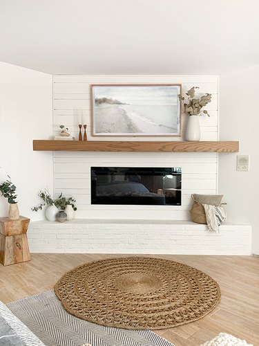simple living room with white brick fireplace, wooden shelf and jute and sisal decor