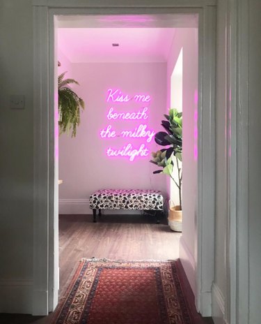 white hallway with large pink neon and ottoman