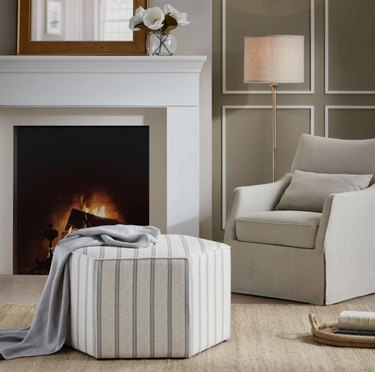 Striped ottoman, accent chair, fireplace, mantle.