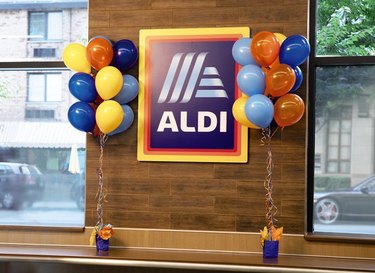 Aldi logo on a wooden wall next to windows surrounded by blue, orange, and yellow balloons.