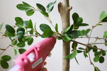 Hot gluing faux green leaves to tree branches
