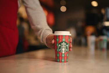person placing red-and-green starbucks cup on table
