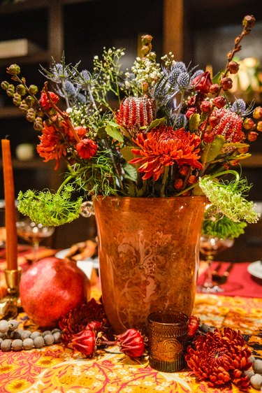 A vase of fresh flowers surrounded by candles, pomegranates, and other florals on a table.
