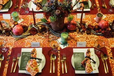 A Friendsgiving tablescape featuring place settings, fresh flowers, pomegranates, and candles.