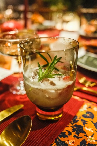 A drink with a sprig of rosemary on top in a clear glass on a red placemat.