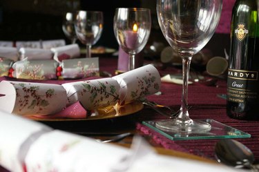 A table setting featuring a white Christmas cracker with holly illustrations on a dinner plate.