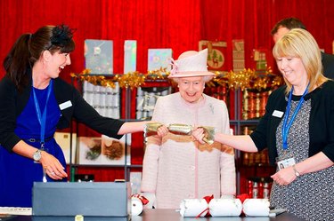 Queen Elizabeth II watching a gold Christmas cracker being pulled open.