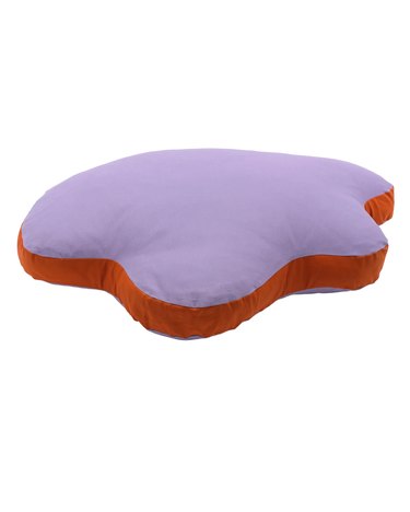 An irregular-shaped dog bed in a light purple with a burnt orange edge.