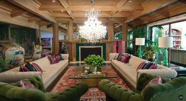 Large living room with white and green couches, red rug, glass coffee table, and crystal chandelier