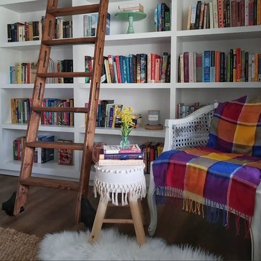 Wooden ladder, low stool, and reading chair next to a white bookshelf