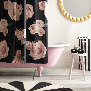 black shower curtain with pink roses over a pink tub in a white bathroom