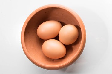 Three brown eggs in a brown bowl