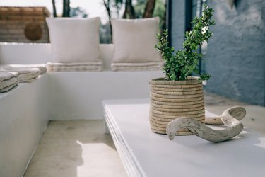 A woven basket with a plant next to a small sculpture on a white coffee table in front of a white couch.