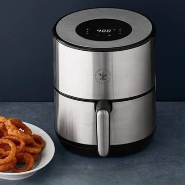 A black air fryer next to a plate of onion rings