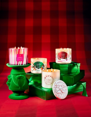 An array of green presents against a red buffalo check background with four Bath and Body Works 3-wick candles shown: Snowy Peach Berry, Vanilla Bean Noel, The Perfect Christmas and Winter Candy Apple