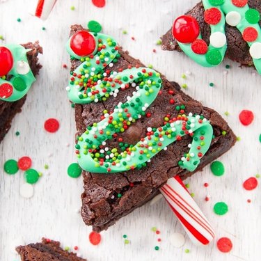 Christmas tree-shaped brownies with green frosting, sprinkles, and a candy cane trunk.