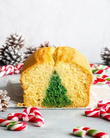 A loaf cake with a green Christmas tree shape on the inside surrounded by candy canes.