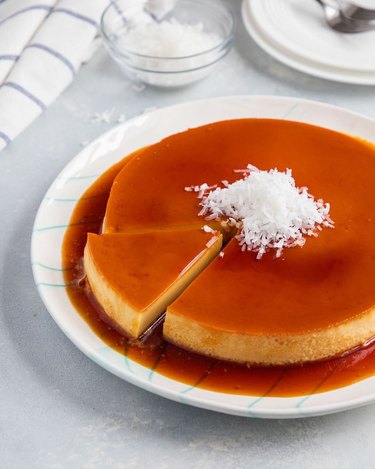 A coconut flan on a white plate with a slice cut on the left side.