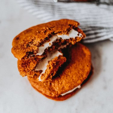 Two gingerbread whoopie pies stacked on top of each other with a bite taken out of the top one.