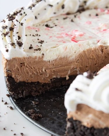 A close-up of peppermint cheesecake with an Oreo crust and a piece missing from the side.
