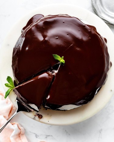 Chocolate cake on a white plate topped with mint leaves.