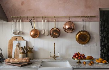 pink kitchen with copper pots hanging from brass utensil rack