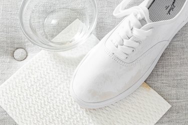 A stained white tennis shoe is on top of a white dish cloth and next to a bowl of white vinegar