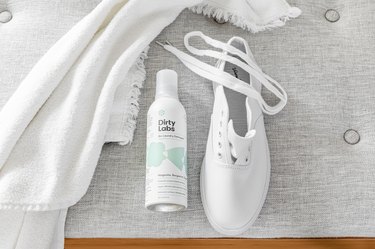 Cleaning white tennis shoes with laundry detergent; a white shoe is staged next to Dirty Labs detergent on a gray bench
