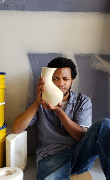 Altarik Banks, a Black person white short black hair holding a tall curvy, light-colored clay vase.