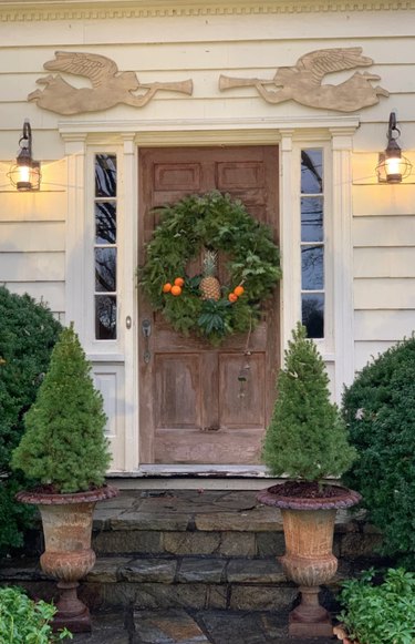 Front door with wreath, angels and pine trees in urns.
