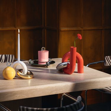 A variety of uncommon matters and H&M home pieces adorn a wooden table with zebra printed chairs. The pieces include a round yellow trinket container, a white and gold taper candle holder, a red and silver taper candle holder and a pink trinket container.