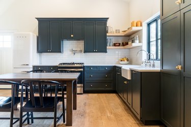 Dark gray cabinets, open shelves, wood floors, apron sink, dining table and chairs.