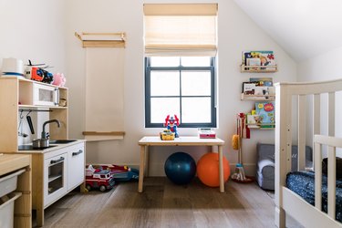 Kid's bedroom with crib, table, books, window, blinds, wood floor.