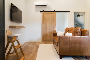 Minimalist living room with a brown sofa, flatscreen tv, wood highchair, and sliding wood barn door