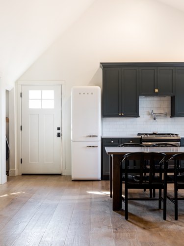 White door, dark cabinets, white refrigerator, dining table and chairs, wood floor.