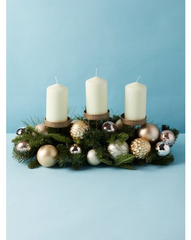 three white candles on evergreen centerpiece with metallic ornaments