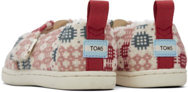The back of a pair of West Elm x TOMS slippers in a green, pink, white and red pattern with TOMS labels on the heels