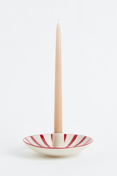 A red and white striped candle holder with a beige candle in it.