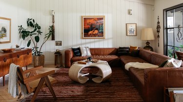 A living room with a brown leather couch, wood and rattan armchair, and sculptural white coffee table.