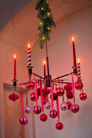 A chandelier featuring red, pink, and red and white striped candles draped in red and red ornaments.