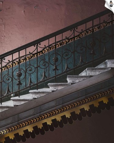 A stairway with a muted red and blue wall and a yellow and brown wallpaper border going up the stairs.