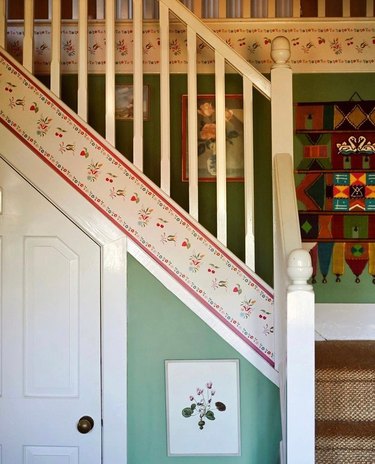 A white staircase with green walls and a red floral wallpaper border going up the stairs.