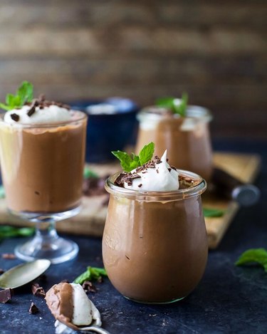 Three glasses of peppermint chocolate mousse on a navy blue tablecloth.