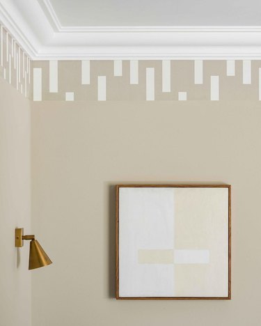 A beige wall and a white and beige painting with a beige and white wallpaper border meeting the white ceiling.