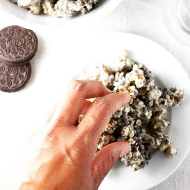 Hand reaching onto a white plate topped with cookies and cream popcorn.