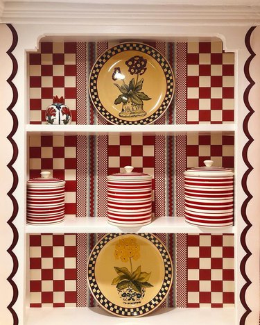A kitchen cabinet with red checkered backsplash and yellow floral plates.