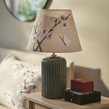 A beige floral lampshade on a green base in a bedroom.